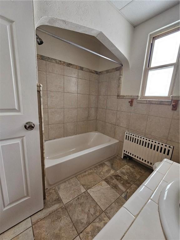 bathroom featuring tile walls, radiator heating unit, and tiled shower / bath