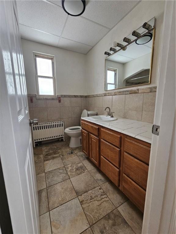 1732 Pennsylvania Ave, West Mifflin, PA 15122 - bathroom with radiator heating unit, vanity, toilet, a drop ceiling, and tile walls