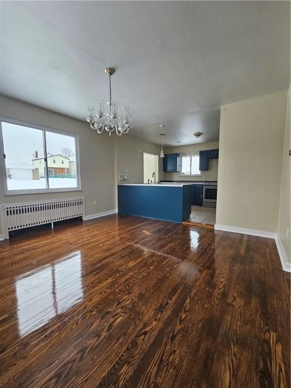 unfurnished living room with an inviting chandelier, radiator heating unit, dark hardwood / wood-style flooring, and sink