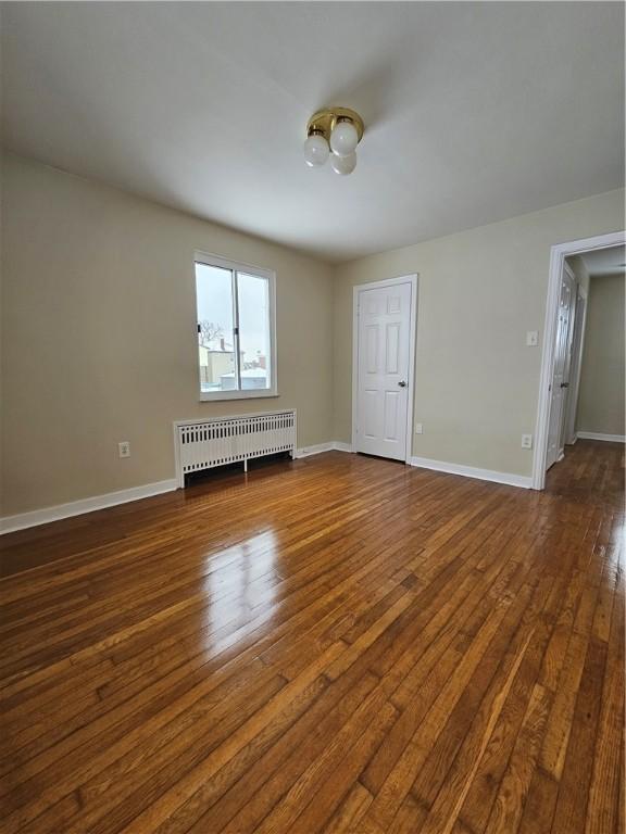 empty room with dark hardwood / wood-style flooring and radiator heating unit