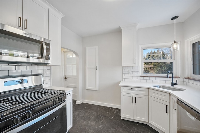 kitchen featuring pendant lighting, sink, appliances with stainless steel finishes, white cabinets, and decorative backsplash