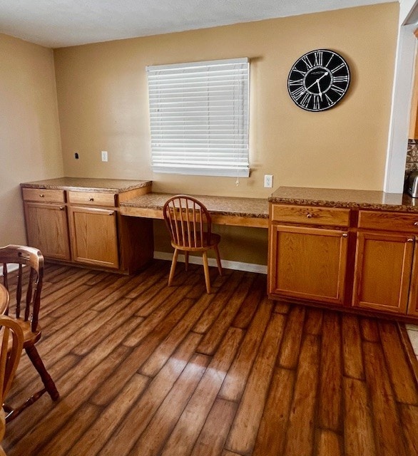 unfurnished office featuring dark hardwood / wood-style flooring and built in desk