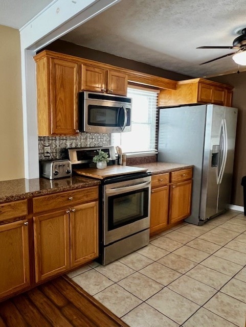 kitchen featuring light hardwood / wood-style flooring, ceiling fan, backsplash, stainless steel appliances, and dark stone counters