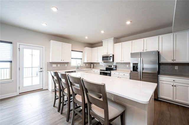 kitchen with a kitchen island, appliances with stainless steel finishes, white cabinetry, a kitchen breakfast bar, and decorative backsplash