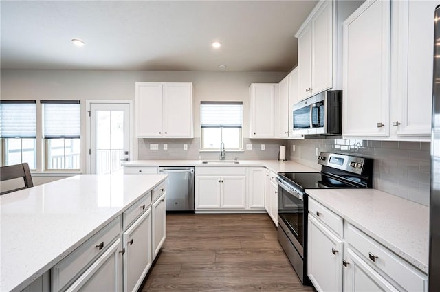 kitchen with sink, appliances with stainless steel finishes, light stone counters, white cabinets, and decorative backsplash