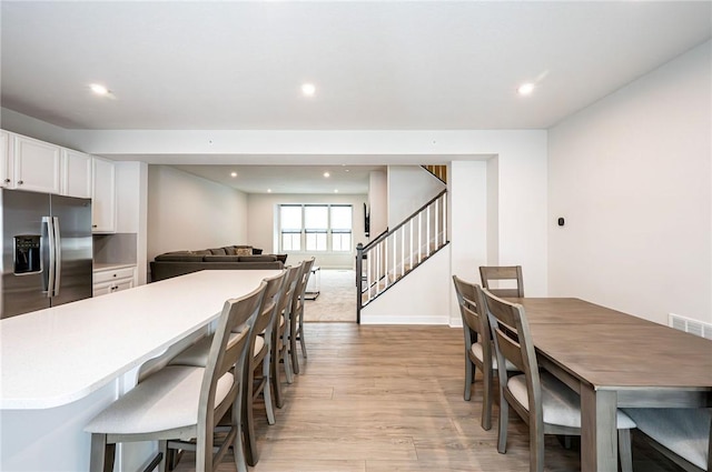 kitchen featuring a breakfast bar area, light hardwood / wood-style floors, white cabinets, and stainless steel refrigerator with ice dispenser