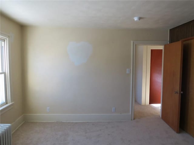 empty room featuring light carpet, radiator heating unit, and plenty of natural light