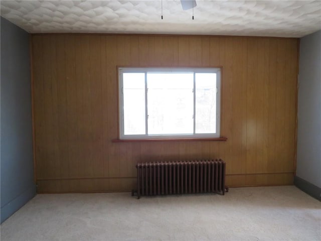 spare room featuring radiator heating unit, light colored carpet, wooden walls, and ceiling fan