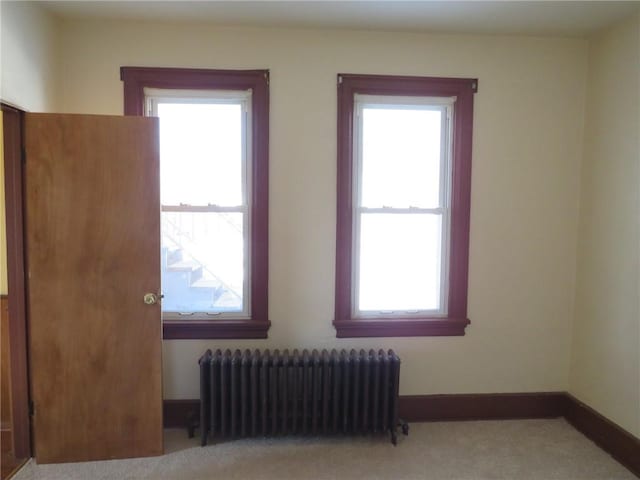 carpeted empty room featuring a wealth of natural light and radiator heating unit