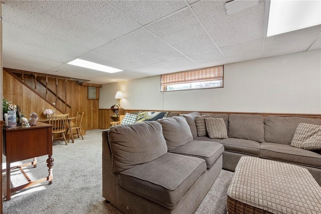 living room with carpet, a drop ceiling, and wooden walls