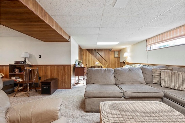 carpeted living room featuring a drop ceiling and wood walls