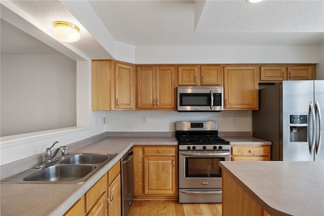 kitchen with appliances with stainless steel finishes, sink, a textured ceiling, and light wood-type flooring