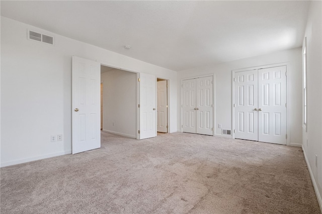 unfurnished bedroom with two closets and light carpet