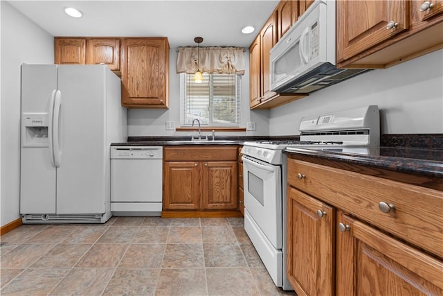 kitchen featuring dark stone countertops, sink, white appliances, and decorative light fixtures