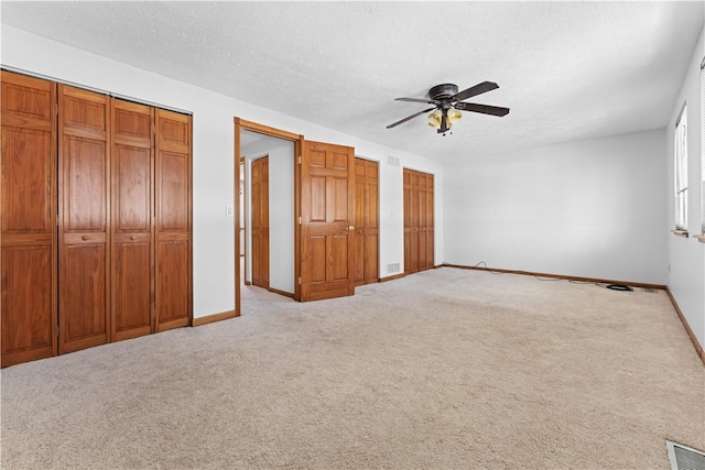 unfurnished bedroom with light carpet, multiple closets, and ceiling fan