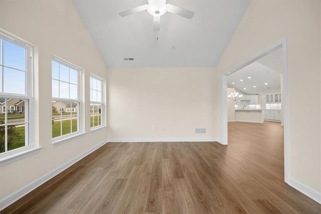 empty room featuring lofted ceiling, hardwood / wood-style floors, and ceiling fan with notable chandelier