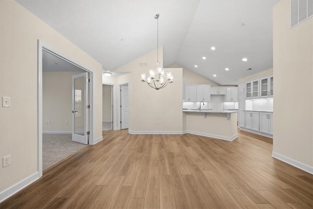 unfurnished living room featuring sink, vaulted ceiling, light hardwood / wood-style floors, and a chandelier