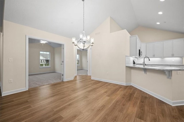 unfurnished dining area featuring lofted ceiling, sink, a notable chandelier, and light wood-type flooring