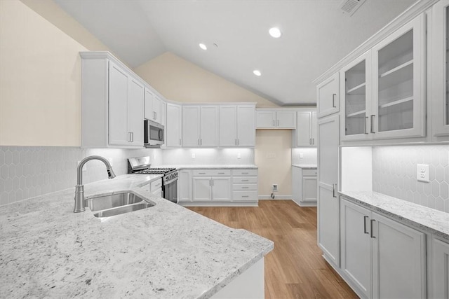 kitchen with white cabinetry, lofted ceiling, sink, stainless steel appliances, and light stone countertops