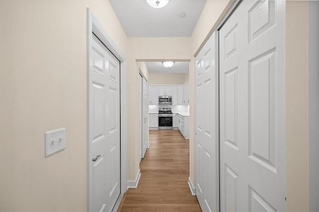 hallway with a textured ceiling and light hardwood / wood-style floors