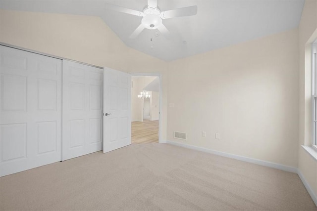 unfurnished bedroom with light carpet, ceiling fan with notable chandelier, lofted ceiling, and a closet