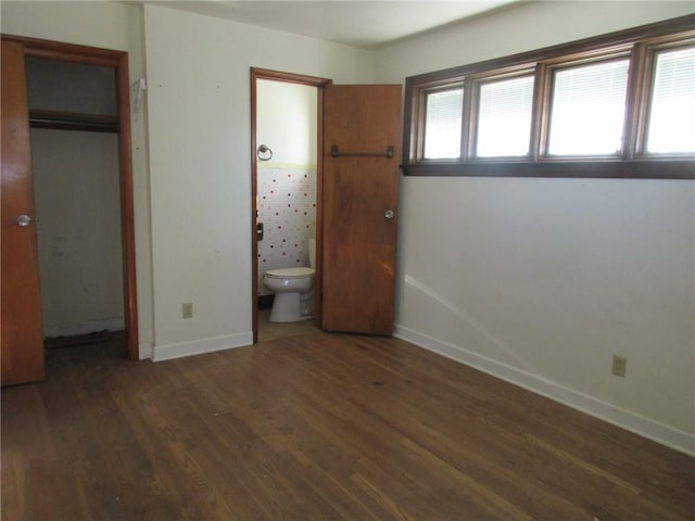 unfurnished bedroom featuring ensuite bathroom, dark hardwood / wood-style floors, and a closet