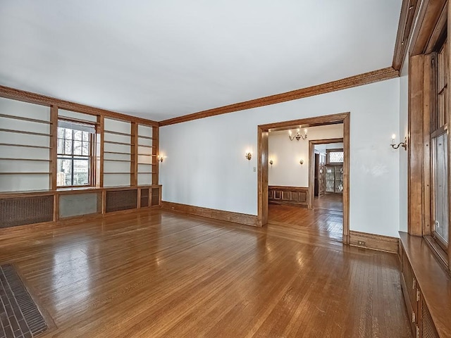 empty room with a notable chandelier, hardwood / wood-style floors, crown molding, and built in features