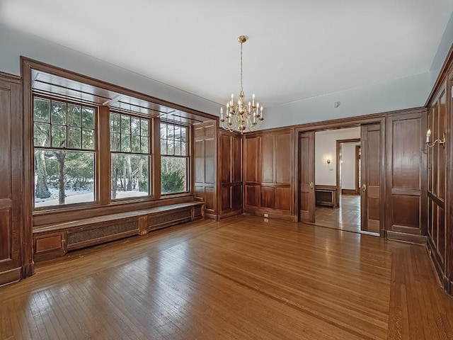 unfurnished dining area with hardwood / wood-style flooring, an inviting chandelier, and a baseboard heating unit