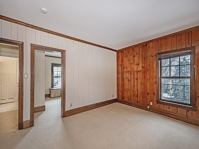 carpeted empty room with a baseboard heating unit, a wealth of natural light, ornamental molding, and wood walls