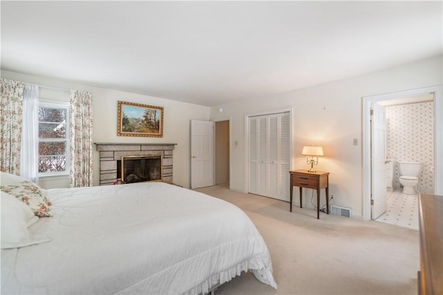 bedroom featuring light carpet, ensuite bath, a fireplace, and a closet