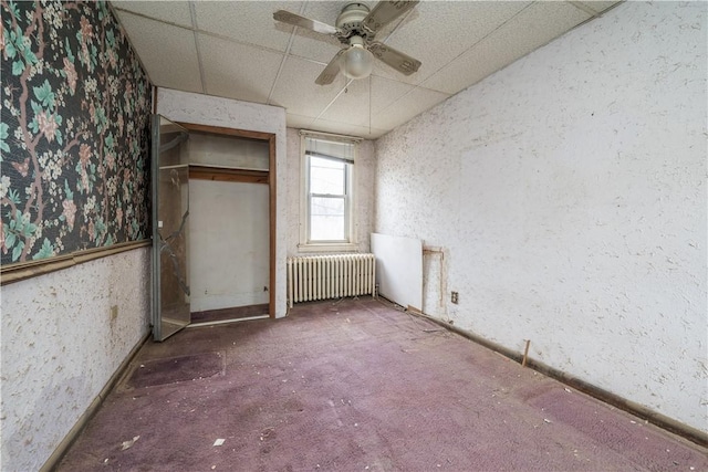 empty room with radiator heating unit, ceiling fan, and a paneled ceiling