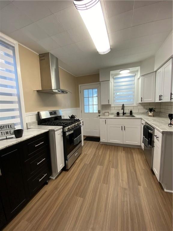 kitchen with wall chimney exhaust hood, stainless steel appliances, sink, and white cabinets