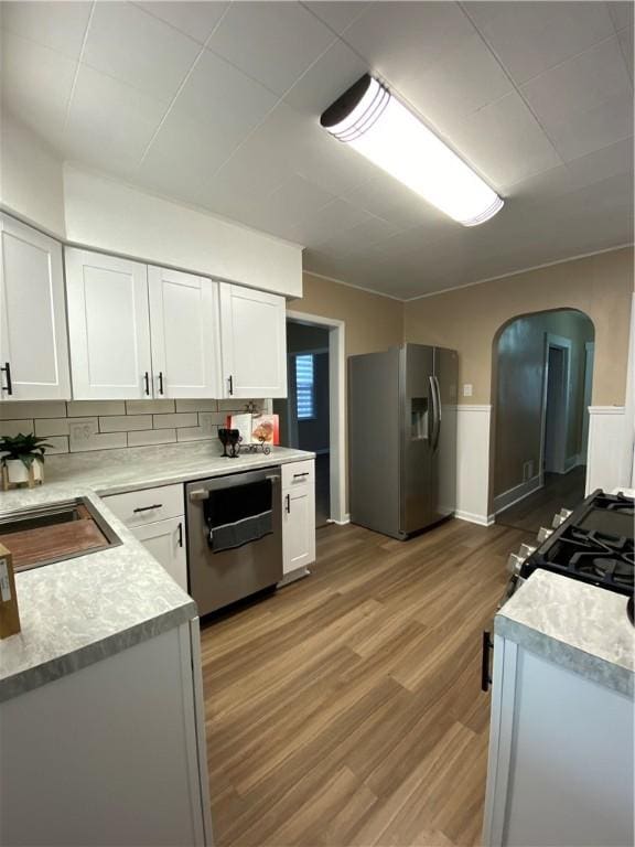 kitchen featuring sink, stainless steel appliances, hardwood / wood-style floors, decorative backsplash, and white cabinets