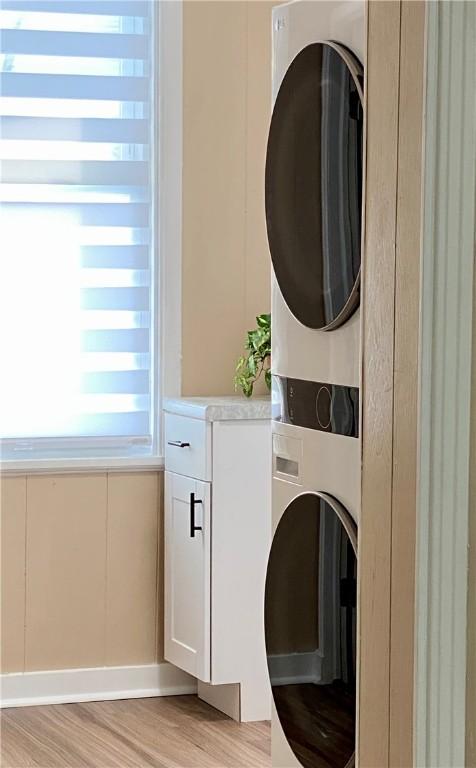 laundry room featuring light hardwood / wood-style floors, cabinets, and stacked washing maching and dryer