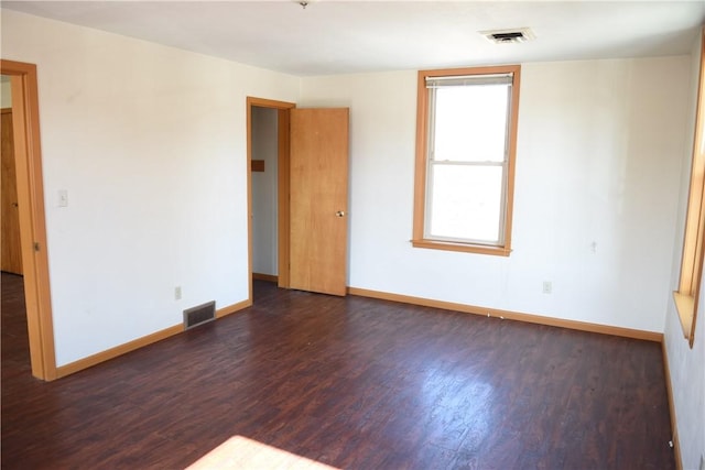 spare room featuring dark wood-style flooring, visible vents, and baseboards