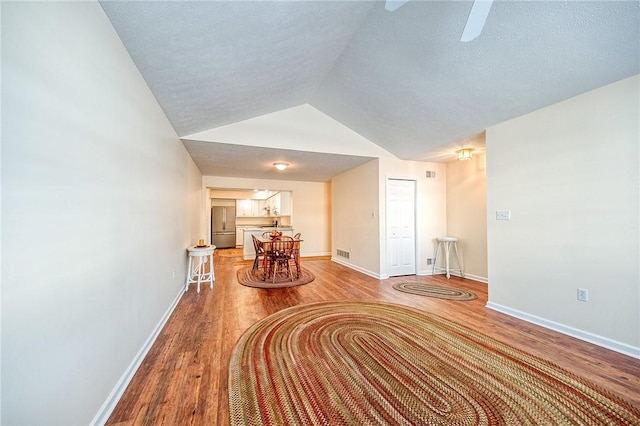 corridor with vaulted ceiling, hardwood / wood-style floors, and a textured ceiling