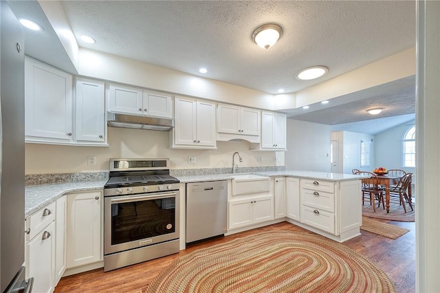 kitchen with stainless steel appliances, sink, white cabinets, and light hardwood / wood-style flooring