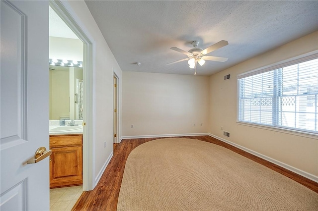 bedroom featuring sink, ensuite bath, light hardwood / wood-style flooring, a textured ceiling, and ceiling fan