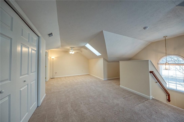 additional living space featuring ceiling fan, vaulted ceiling with skylight, light colored carpet, and a textured ceiling