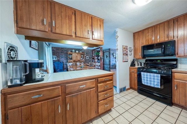 kitchen featuring brick wall, tile countertops, light tile patterned floors, and black appliances