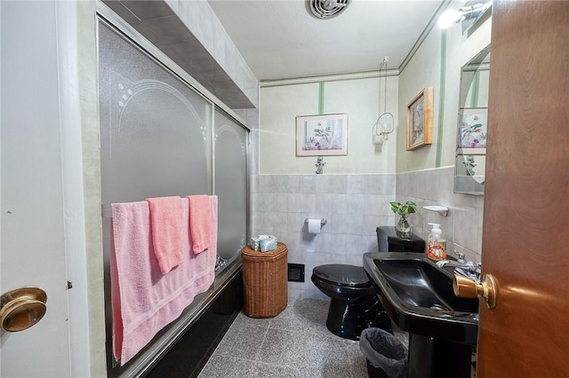 full bathroom with tile walls, sink, bath / shower combo with glass door, and toilet