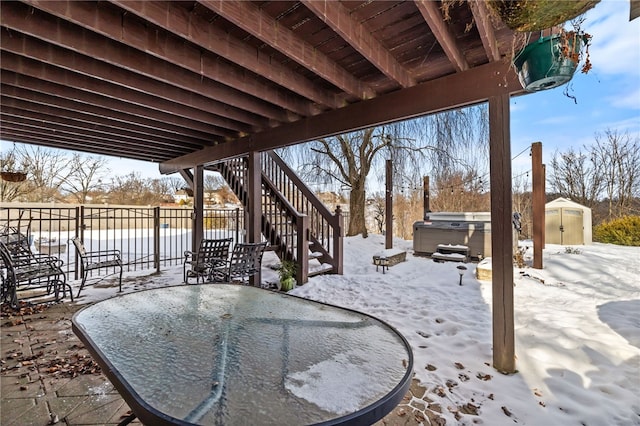 snow covered patio featuring a hot tub and a storage shed