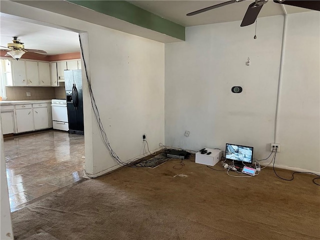 interior space featuring white range with gas stovetop, black fridge, white cabinets, ceiling fan, and backsplash