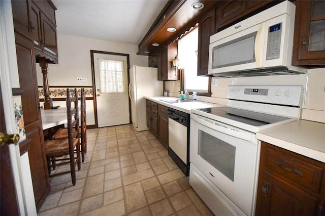 kitchen with dark brown cabinetry, sink, white appliances, and a wealth of natural light