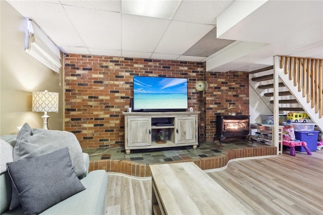 living room featuring hardwood / wood-style flooring, brick wall, and a drop ceiling