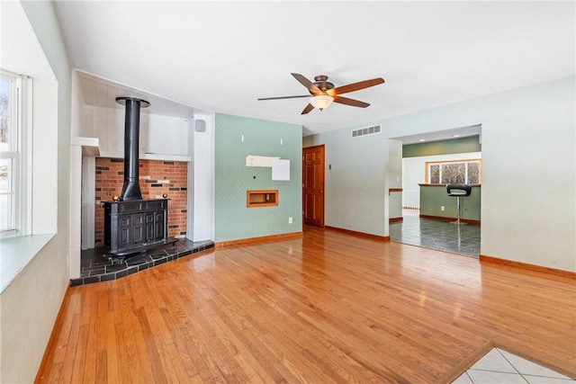 unfurnished living room featuring light hardwood / wood-style flooring, ceiling fan, and a wood stove