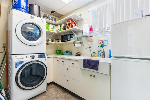 laundry area featuring sink, light tile patterned flooring, cabinets, and stacked washing maching and dryer