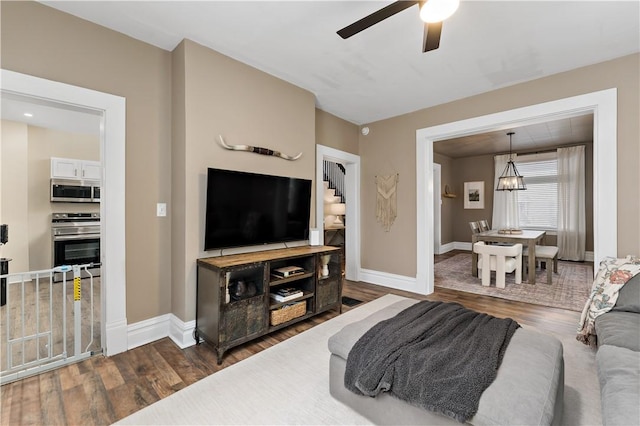 living room with ceiling fan with notable chandelier and dark wood-type flooring