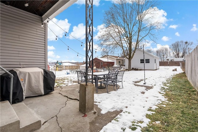 snow covered patio featuring a grill and an outbuilding