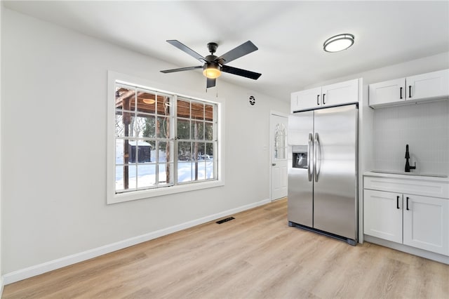 kitchen with sink, white cabinetry, light hardwood / wood-style flooring, stainless steel fridge, and backsplash